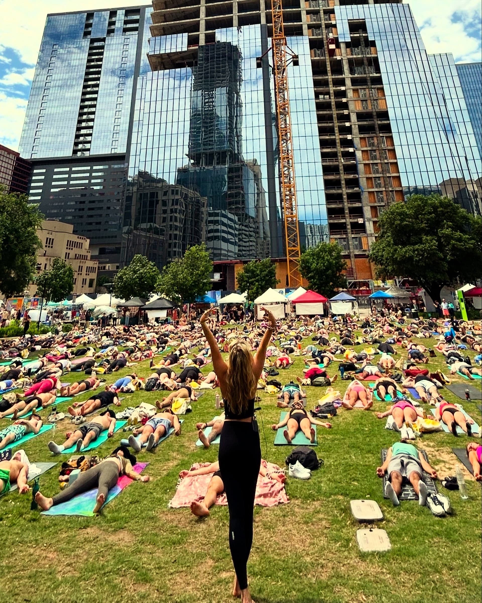 Liz standing over a huge downtown savasana class, arms raised